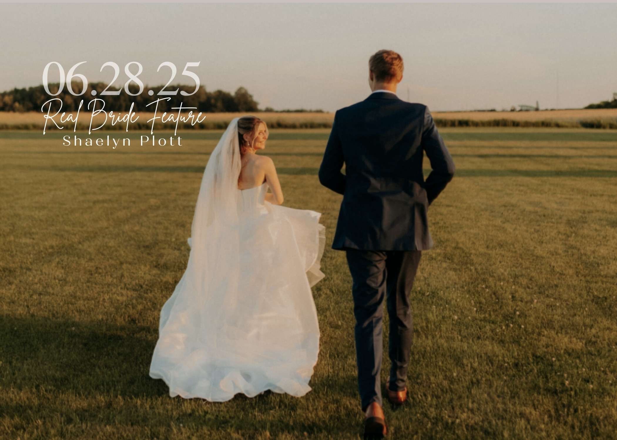 Bride Shaelyn Plott walking across a sunlit field in a flowing wedding gown and veil, holding her train while looking back at the camera, with her groom walking beside her.