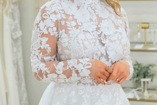 A woman wearing a white lace wedding dress with long sleeves, featuring intricate floral patterns, perfectly highlights the elegance often discussed in a wedding dress fabric guide.