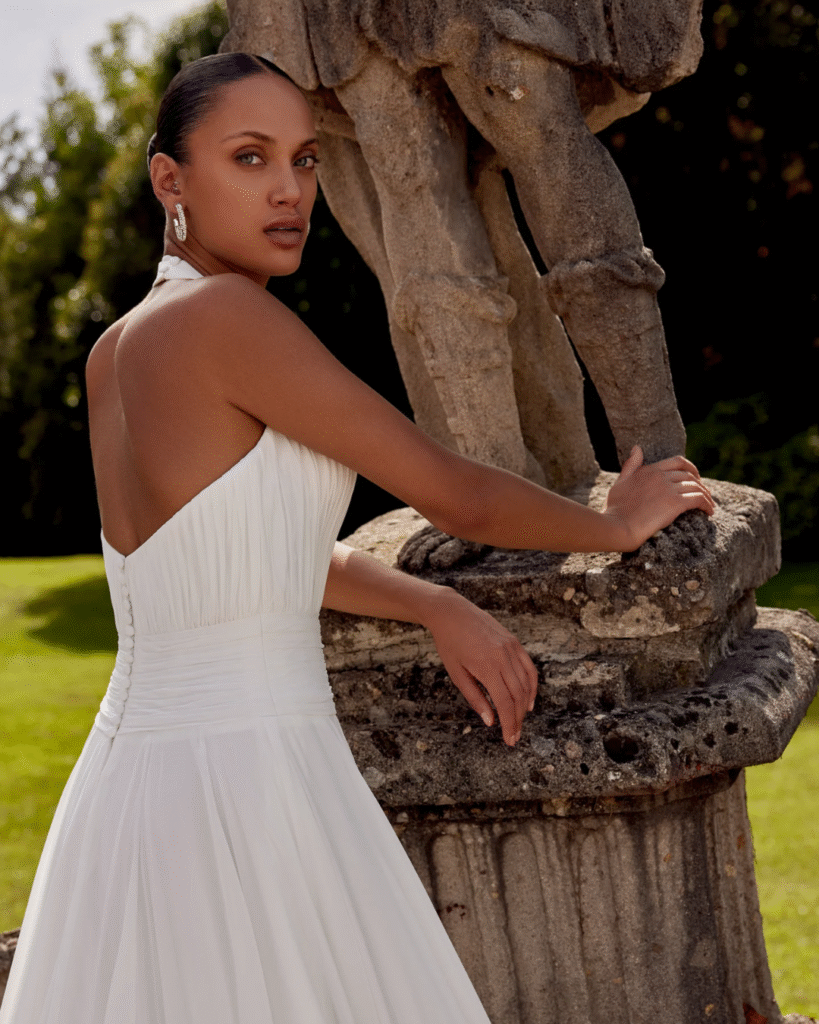 A bride beside a statue wearing a white halter dress