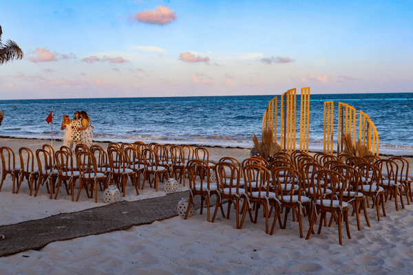 Chairs arranged on the beach for a wedding ceremony, with ocean behind and decorative wooden backdrop.