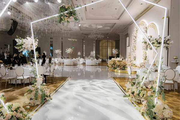 A beautifully decorated event venue with a white aisle, tables, and floral arrangements.