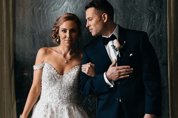 A bride in a sparkling white dress stands next to a groom in a black suit, full of elegance.