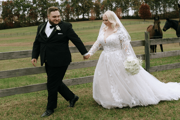 A bride and groom holding hands with horses in the background