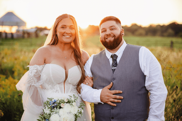 the bride and groom with coordinating looks smiling in front of the camera at sunset