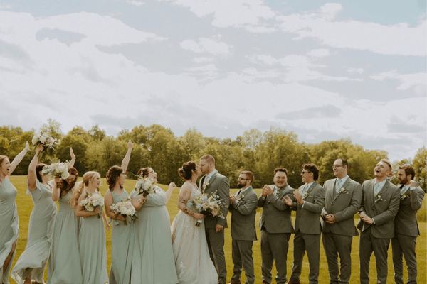 Bride and groom kissing while their bridal party cheers, wearing coordinated tuxedo and bridesmaid dress colors.