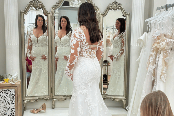 Bride standing in front of a mirror trying on her wedding dress, with a dress rack beside her