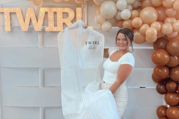 Bride-to-be holding her wedding dress while standing in front of a Twirl Bride backdrop