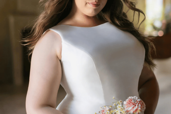A plus size bride in her boat neckline wedding dress holding a bouquet