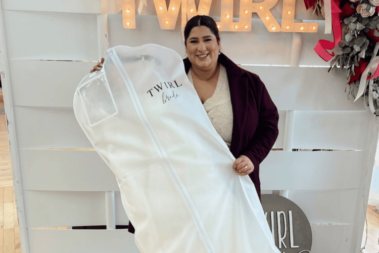 Smiling woman holds a white garment bag labeled "Twirl Bride." She stands in front of an illuminated "Twirl" sign on a bright, modern backdrop.