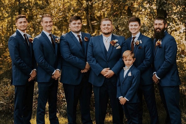 Groom and groomsmen wearing matching blue suits posing outdoors before a wedding ceremony