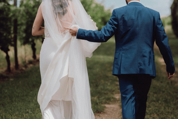 Bride and groom walking outdoors with the groom holding the bride's wedding dress train.