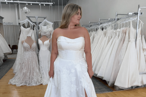 Bride wearing a strapless satin wedding dress in a bridal boutique, surrounded by wedding gowns.
