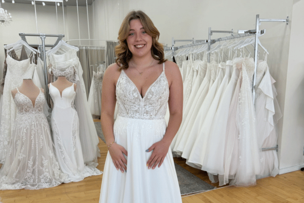 Bride wearing a lace V-neck wedding dress with a full skirt in a bridal boutique.