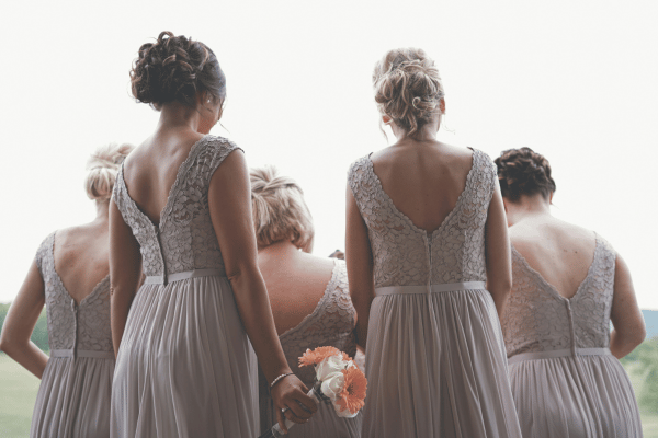 Bridesmaids in light-colored dresses standing together outdoors, holding bouquets.