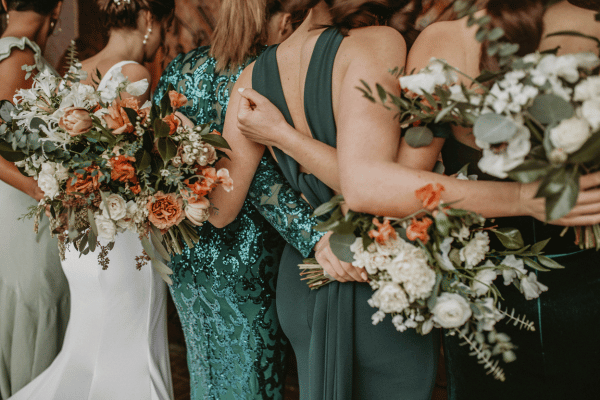 Bridesmaids in green dresses posing together with colorful floral bouquets.