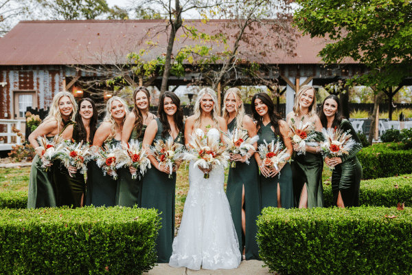 Bride and bridesmaids posing outdoors in matching dark green dresses and holding bouquets.