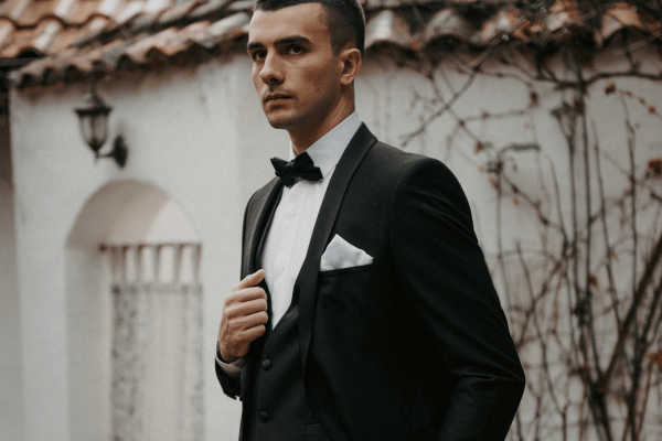 Groom wearing a classic black tuxedo and bow tie, posing outdoors.