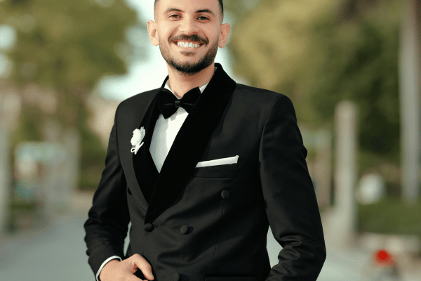 Smiling groom wearing a black double-breasted tuxedo with a bow tie and boutonniere.