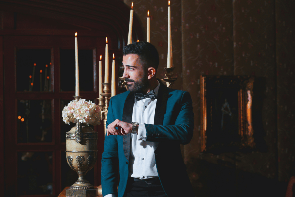Groom wearing a teal tuxedo with a black bow tie in an elegant indoor setting.