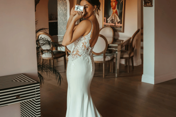 Bride wearing a fitted lace wedding dress with an open back indoors.