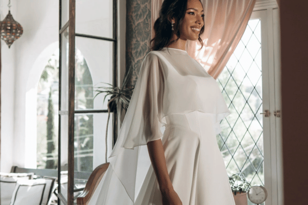 Bride wearing a flowy wedding dress with sheer sleeves in an elegant home setting.