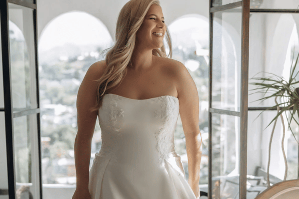 Smiling bride wearing a strapless wedding dress in a bright room overlooking the city.